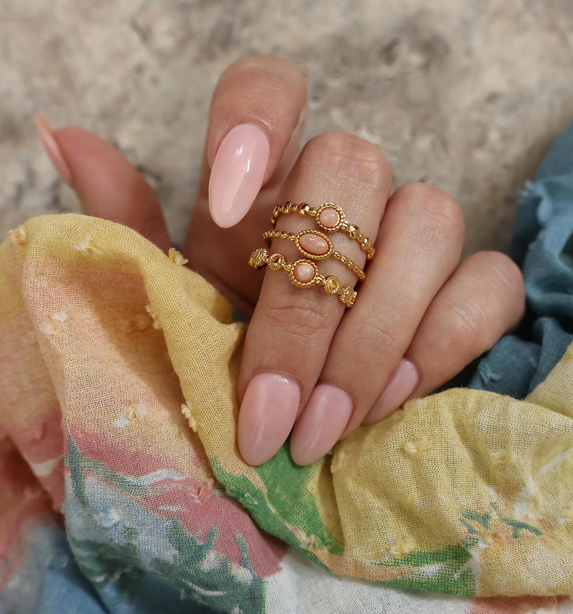 Closeup of hand wearing a gold ring with pink stones holding rainbow fabric