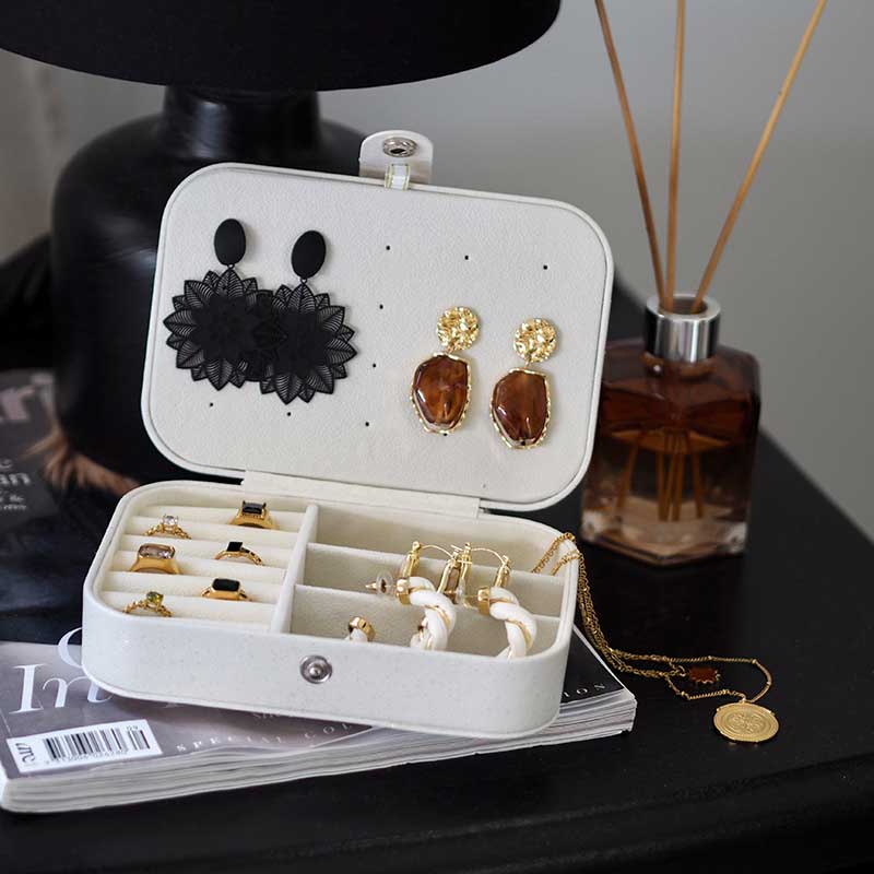 White with shimmering pearl travel case for jewellery on beside table holding various jewellery but in particular the gold and resin Alethea Earrings by Dear Henley