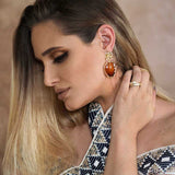 Closeup of woman wearing elegant gold drop earrings with brown acrylic resin, called Alethea Earrings by Dear Henley