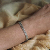 Close-up of jewellery wrist of Woman Wearing Sterling Silver Darcy Bracelet lying on a yellow silk background